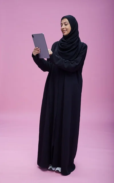Saudi Woman in Abaya Using Tablet on Pink Studio Background