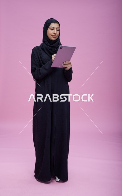 Saudi Woman Using Digital Tablet on Pink Studio Background