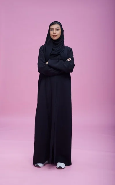 امرأة سعودية بالعباءة والحجاب أمام خلفية وردية