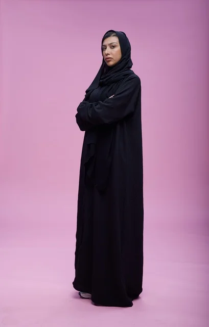امرأة سعودية بالعباءة السوداء أمام خلفية زهرية