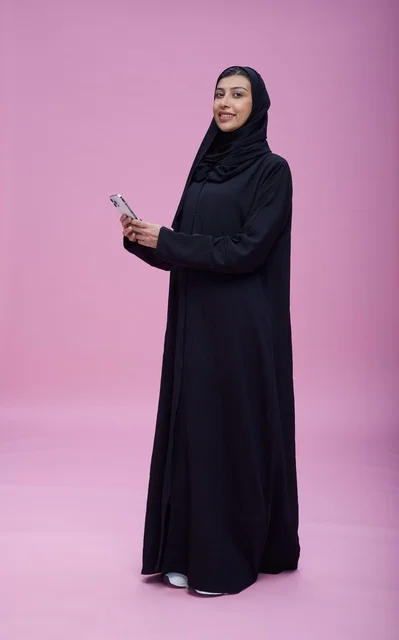 امرأة سعودية تستخدم هاتف ذكي في استوديو بخلفية وردية