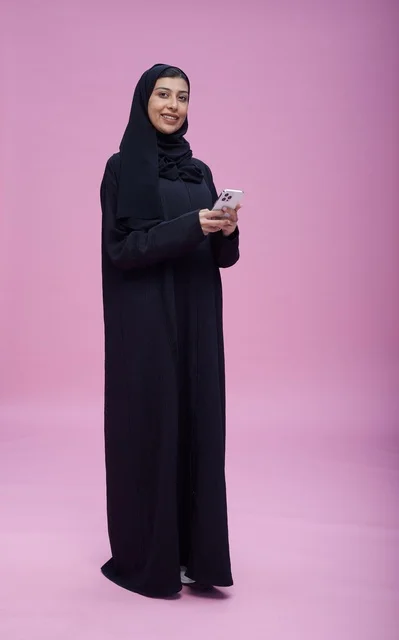 امرأة سعودية في الاستوديو تستخدم الهاتف بخلفية وردية