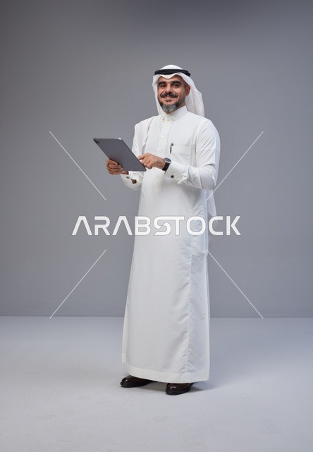 رجل سعودي بالزي التقليدي يستخدم جهازاً لوحياً