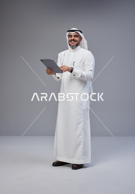 رجل سعودي بالزي التقليدي يستخدم جهازاً لوحياً