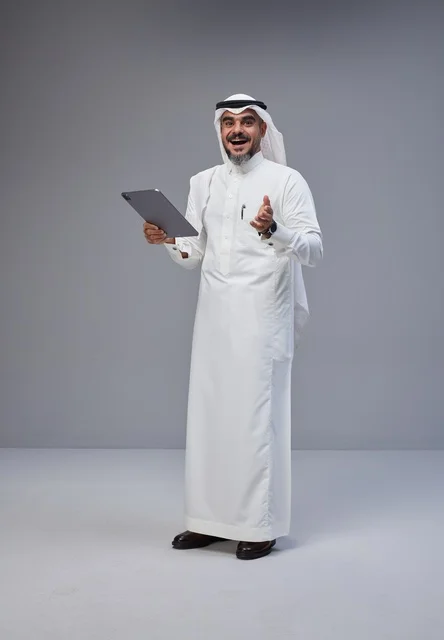 رجل سعودي بالزي التقليدي يمسك جهازاً لوحياً
