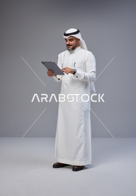 رجل سعودي بالزي التقليدي يستخدم جهازاً لوحياً في الاستوديو