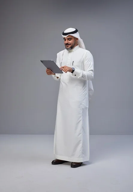 رجل سعودي بالزي التقليدي يستخدم جهازاً لوحياً في الاستوديو
