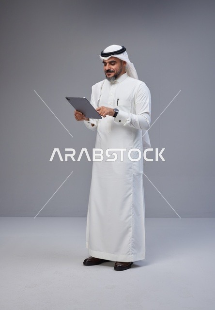Saudi Man in Traditional Thobe Using Tablet in Studio