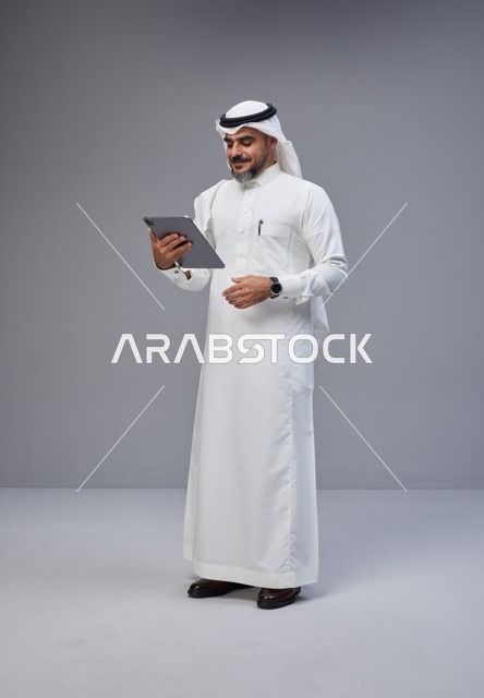 رجل سعودي بالزي التقليدي يستخدم جهازاً لوحياً في الاستوديو
