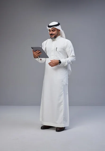 رجل سعودي بالزي التقليدي يستخدم جهازاً لوحياً في الاستوديو