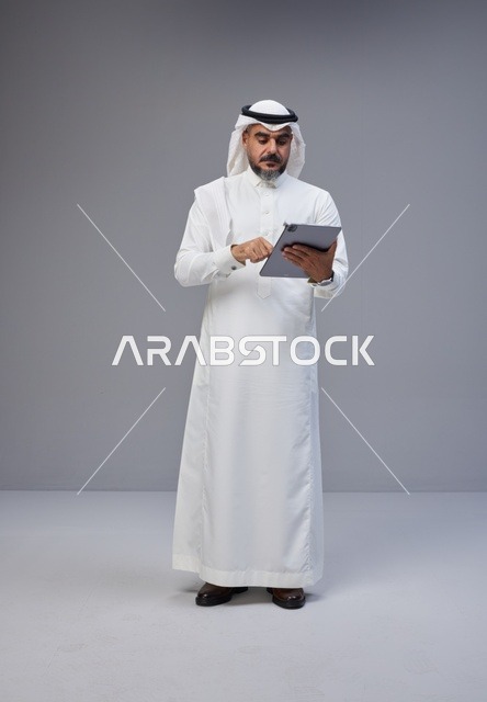 رجل سعودي بالزي التقليدي يستخدم جهازاً لوحياً