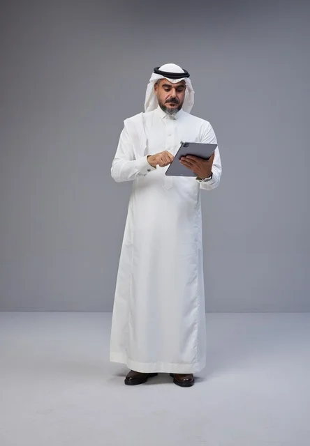رجل سعودي بالزي التقليدي يستخدم جهازاً لوحياً