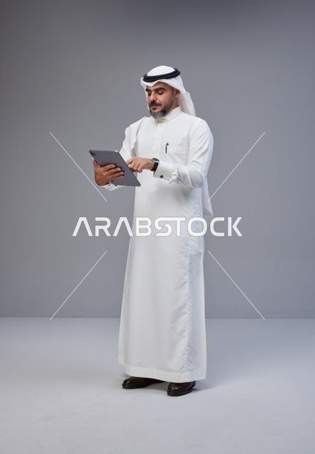 رجل سعودي بالزي التقليدي يستخدم جهازاً لوحياً