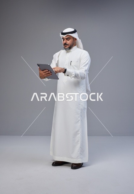رجل سعودي بالزي التقليدي يستخدم جهاز لوحي