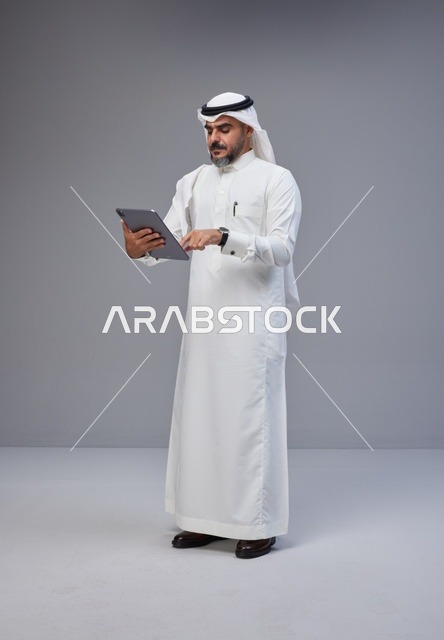 رجل سعودي بالزي التقليدي يستخدم جهازاً لوحياً