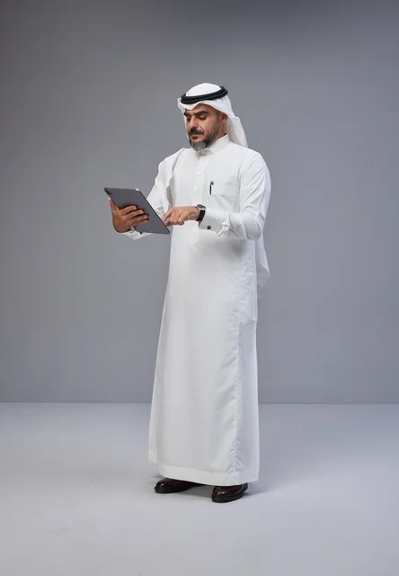 رجل سعودي بالزي التقليدي يستخدم جهازاً لوحياً
