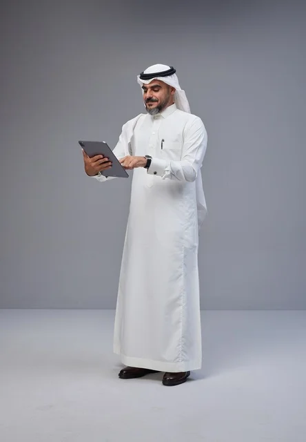 رجل سعودي بالزي التقليدي يستخدم جهازاً لوحياً