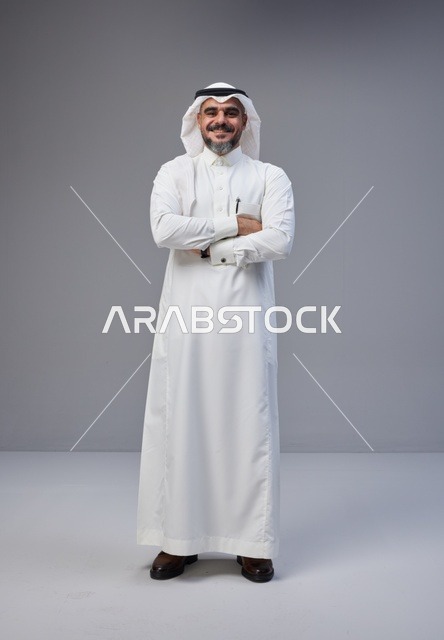 رجل سعودي بالزي التقليدي يقف بثقة بوضعية مكتوفة الأيدي