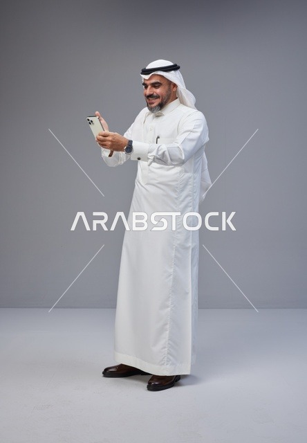 Saudi Man in Traditional Thobe Using Smartphone Studio