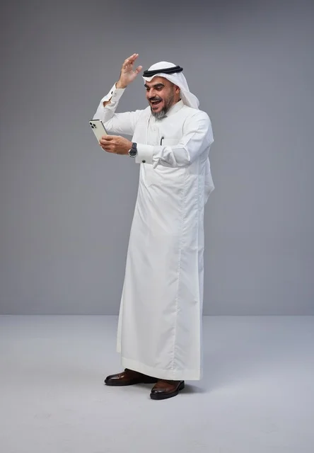 رجل سعودي بالزي التقليدي يستخدم الهاتف الذكي بحماس