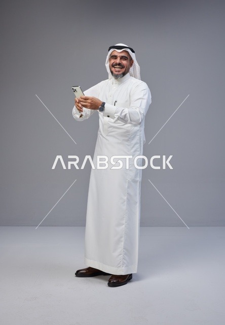Smiling Saudi Man in Traditional Thobe Using Smartphone