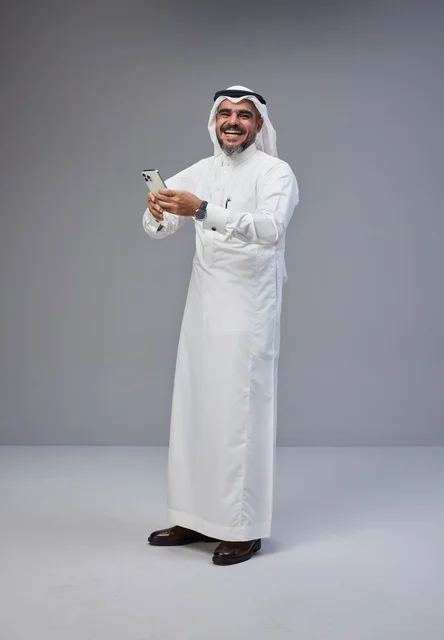 Smiling Saudi Man in Traditional Thobe Using Smartphone