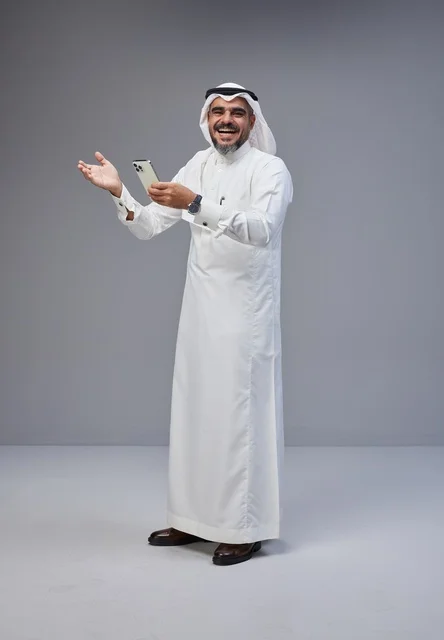 رجل سعودي بالزي التقليدي يستخدم الهاتف الذكي مبتسماً
