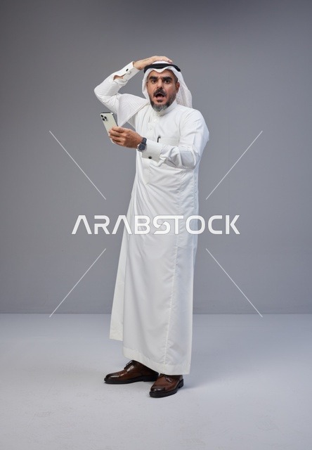 Shocked Saudi Man Using Smartphone on Grey Background