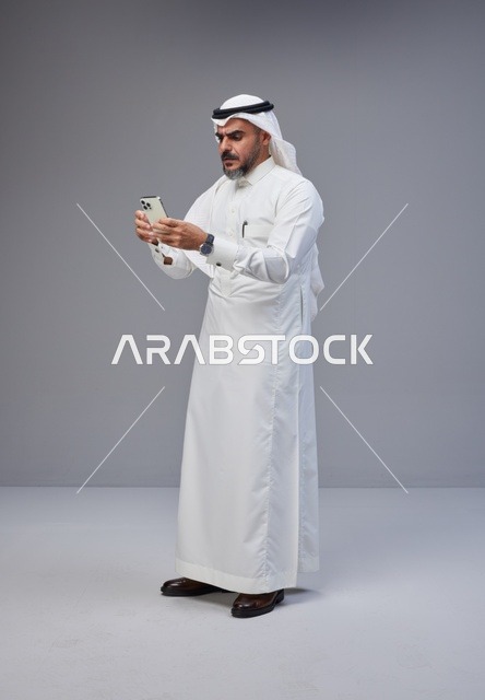 رجل سعودي بالزي التقليدي يستخدم الهاتف الذكي