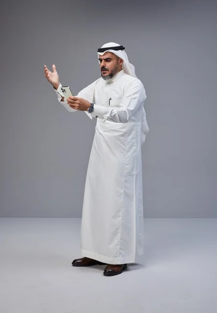 رجل سعودي بالزي التقليدي يستخدم الهاتف الذكي في الاستوديو