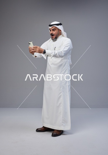 رجل سعودي بالزي التقليدي يستخدم الهاتف الذكي
