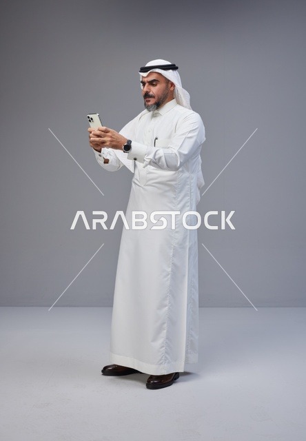 رجل سعودي بالزي التقليدي يستخدم الهاتف الذكي