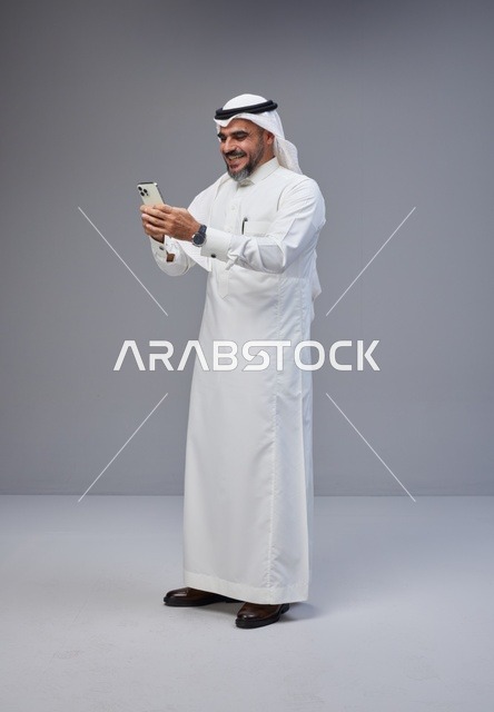 Saudi Man in Traditional Attire Using Smartphone