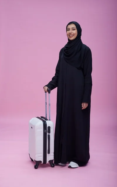 امرأة سعودية بالعباءة مع حقيبة سفر بخلفية وردية