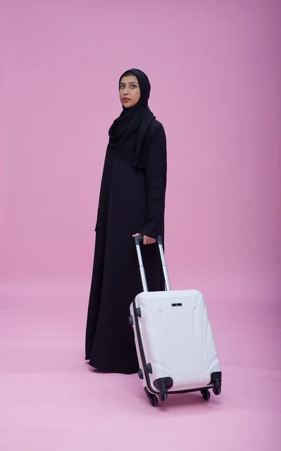 امرأة سعودية بالعباءة مع حقيبة سفر بخلفية وردية