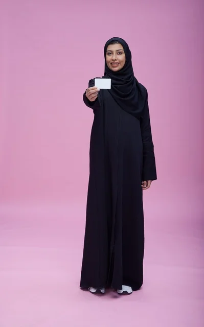 امرأة سعودية بالعباءة تحمل بطاقة فارغة بخلفية وردية