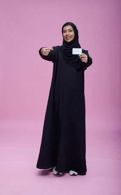 امرأة سعودية محجبة تحمل بطاقة فارغة بخلفية وردية