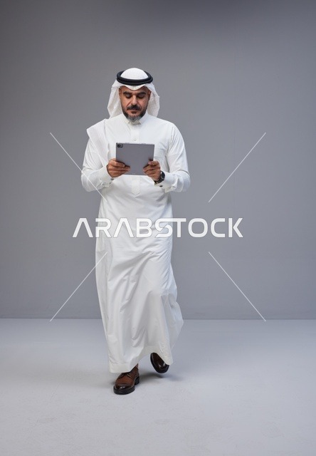 رجل سعودي بالزي التقليدي يستخدم جهازاً لوحياً