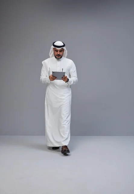 رجل سعودي بالزي التقليدي يستخدم جهازاً لوحياً
