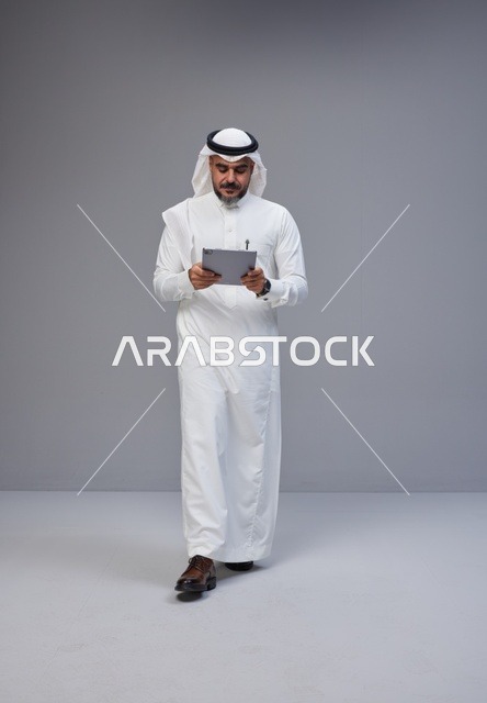 رجل سعودي بالزي التقليدي يستخدم جهازاً لوحياً