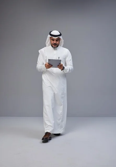 رجل سعودي بالزي التقليدي يستخدم جهازاً لوحياً