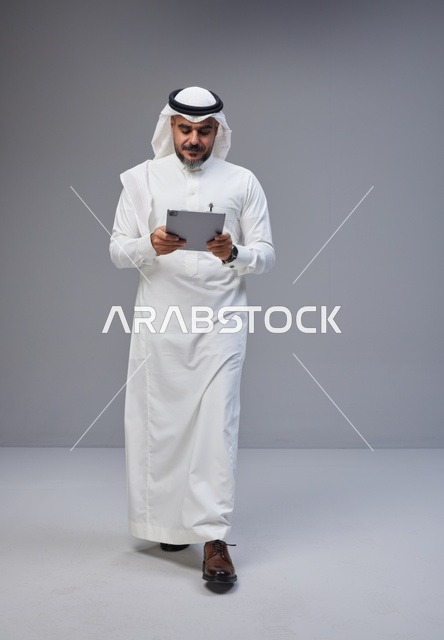 رجل سعودي بالزي التقليدي يستخدم جهازاً لوحياً في استوديو