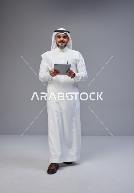 رجل سعودي بالزي التقليدي يستخدم جهازاً لوحياً