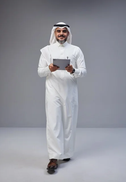 رجل سعودي بالثوب والتابلت في استوديو رمادي