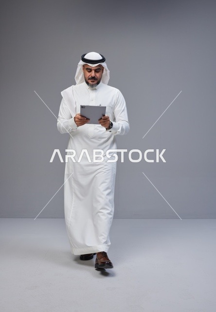 Saudi Man in Traditional Thobe Using Tablet in Studio