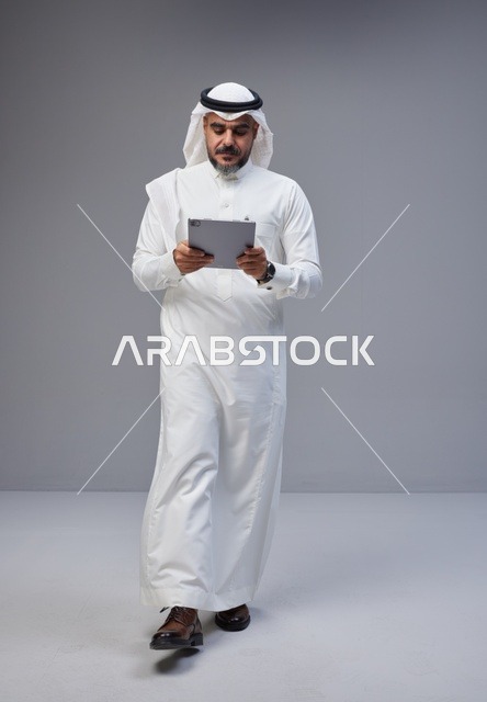Saudi Man in Traditional Thobe Using Tablet in Studio