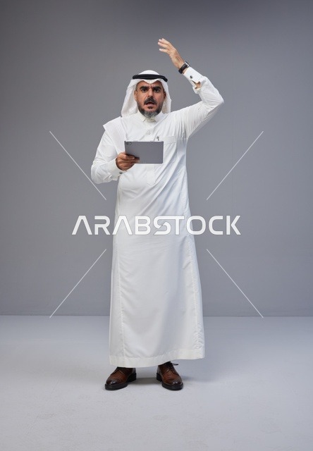 رجل سعودي بزي تقليدي يحمل جهاز لوحي بتعبير متفاجئ