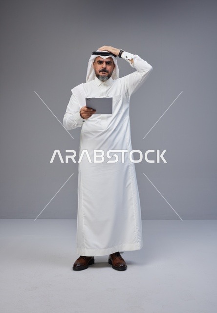 رجل سعودي بالزي التقليدي يستخدم جهازاً لوحياً بتركيز