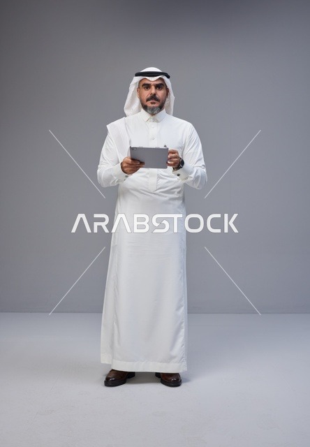 رجل سعودي بالزي التقليدي يستخدم جهازاً لوحياً في الاستوديو