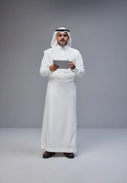 رجل سعودي بالزي التقليدي يستخدم جهازاً لوحياً في الاستوديو